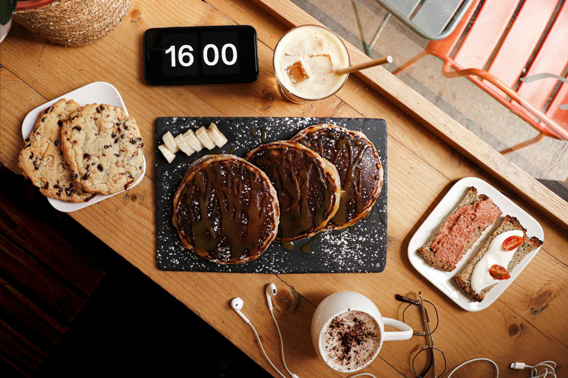 tray of chocolate pancakes served with banana slices between plates of cookies and sandwiches